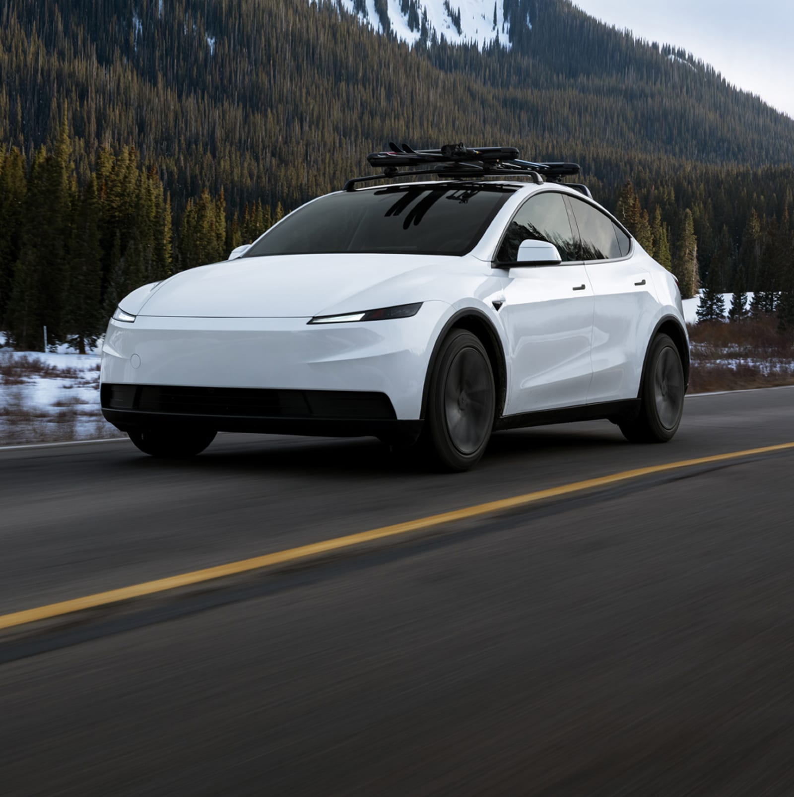 A white Tesla Model Y driving on a mountain road.